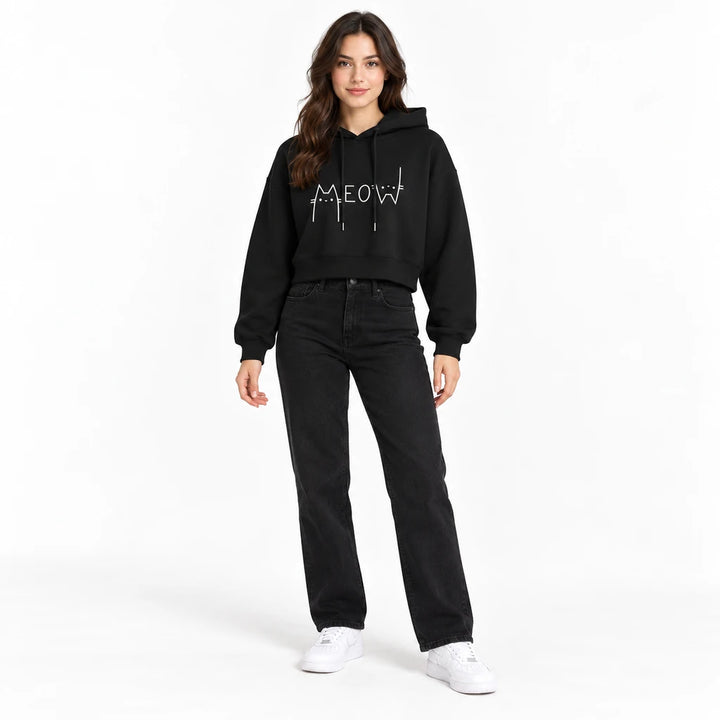Cat cropped hoodie in black on a studio model with black jeans and white sneakers shown full length against a white backdrop.