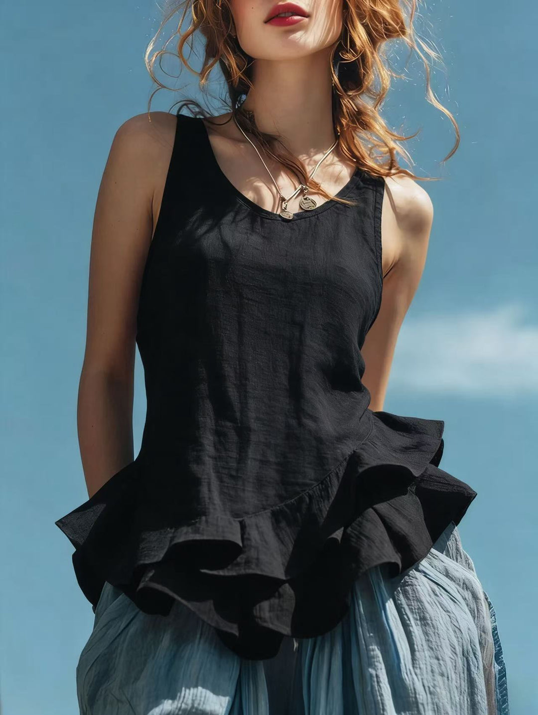 Woman wearing a black top with ruffled details against a blue sky.