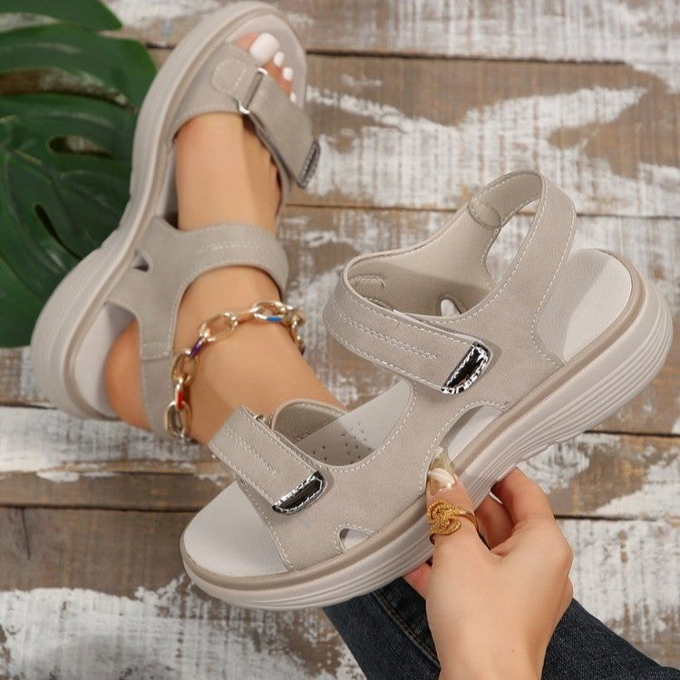 Gray sandals being held up on a wooden surface with a plant in the background