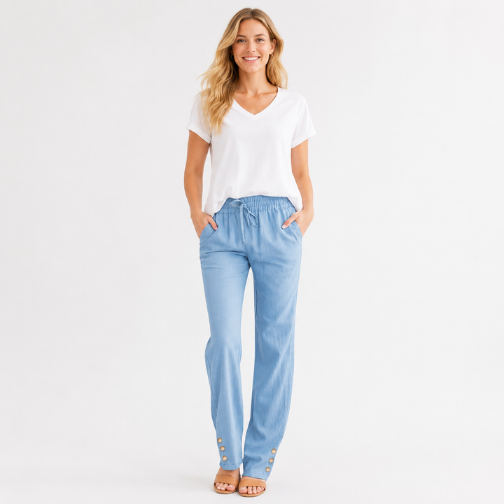 A woman modeling light blue straight-leg pants with a drawstring waist and decorative gold-tone buttons near the hems, paired with a white V-neck t-shirt, on a solid white studio background.