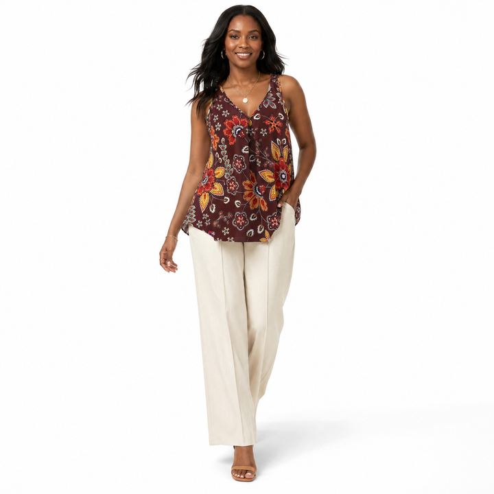 A woman modeling a sleeveless V-neck top with a brown, orange, and red floral paisley print, paired with cream wide-leg pants, on a white studio background.