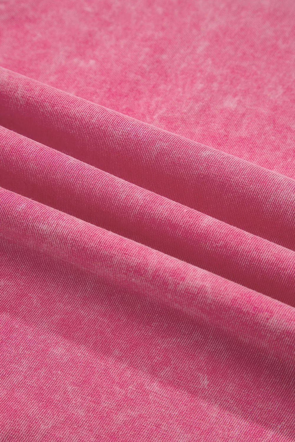 A close-up of pink fabric with a soft, slightly mottled texture, draped in diagonal folds.