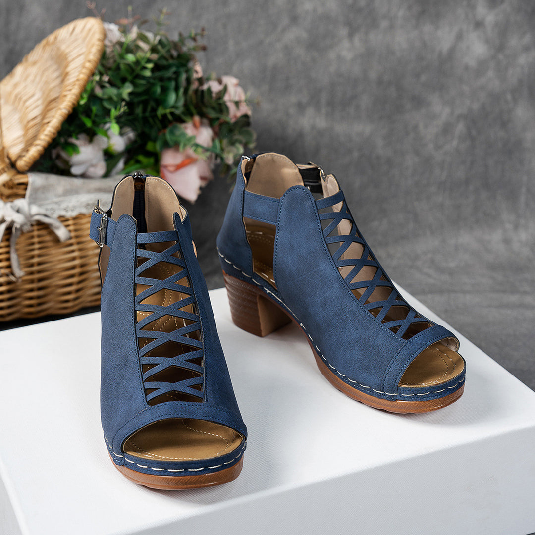 Blue open-toe shoes with brown soles on a white surface, with a blurred background.