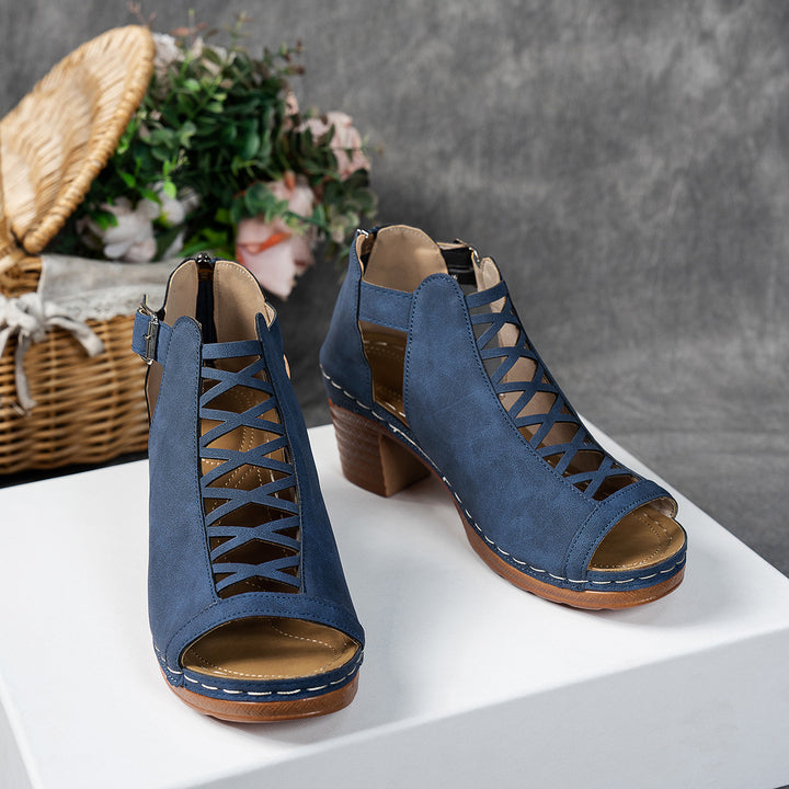Blue open-toe shoes with brown soles on a white surface, with a blurred background.