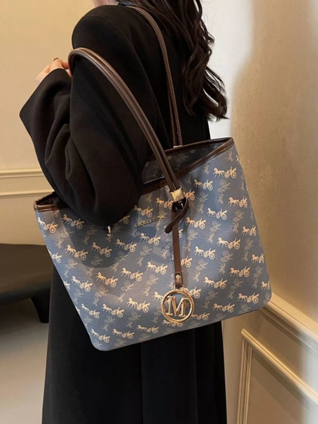 Blue handbag with horse pattern held by a person in a black outfit.