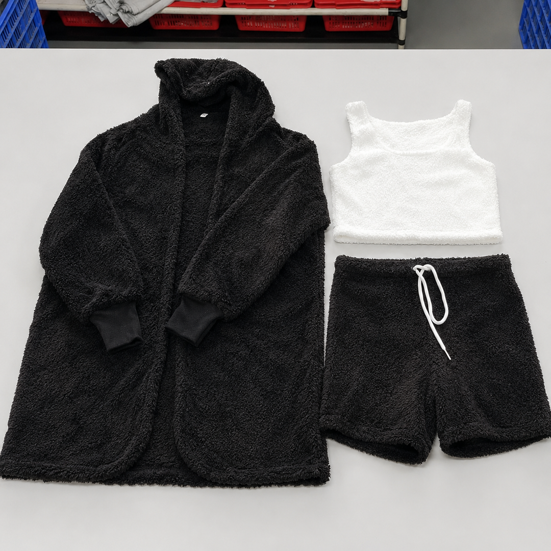 3 piece pajama set women in black with fuzzy hooded cardigan, white crop top and drawstring shorts arranged on a worktable.