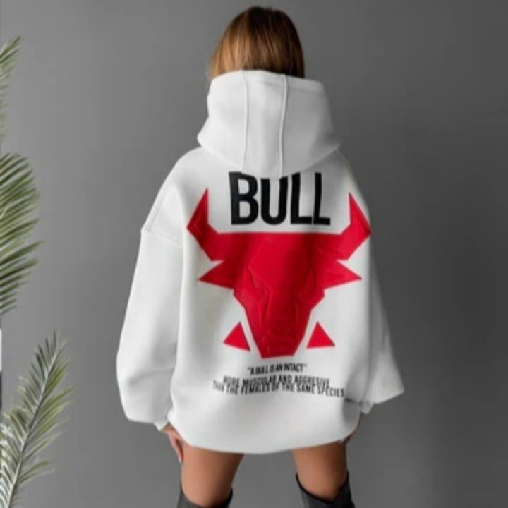 Rear view of a model wearing the white hooded pullover with a red bull graphic and black BULL lettering against the grey wall
