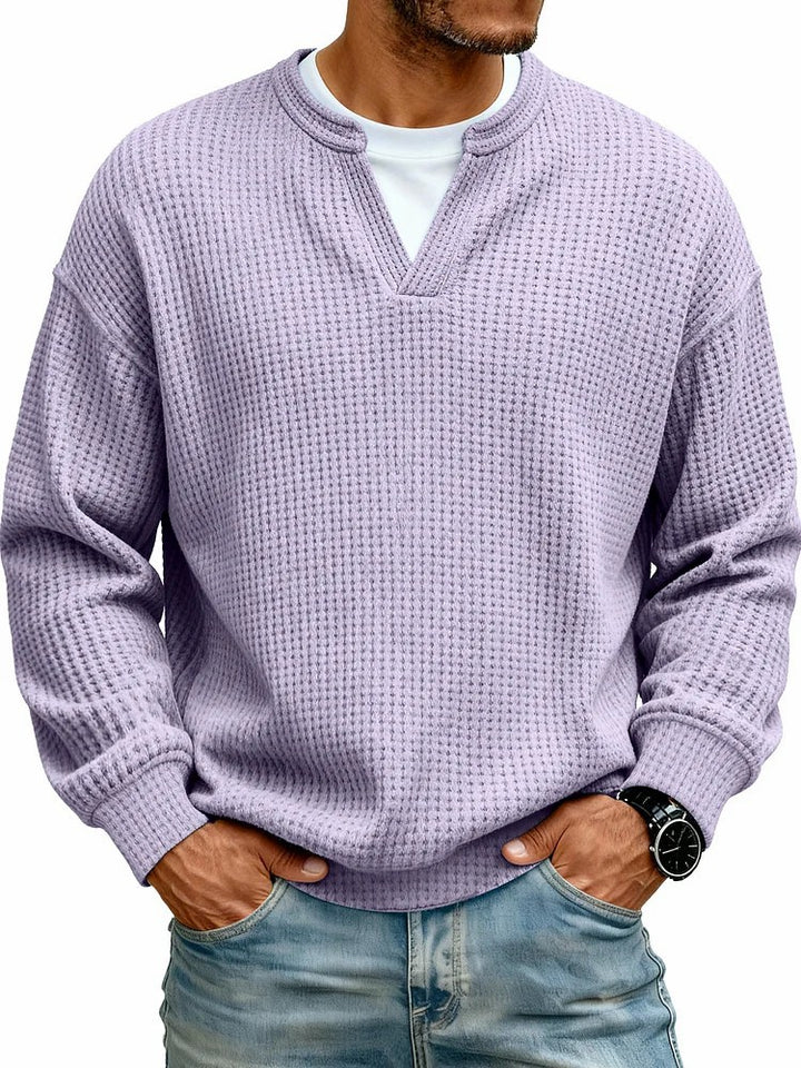 Man wearing a textured purple sweater over a white shirt with blue jeans on a white background