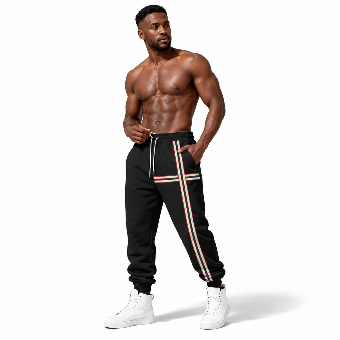 A shirtless muscular man modeling black jogger sweatpants with beige and white side stripes, paired with white high-top sneakers, against a plain white background.