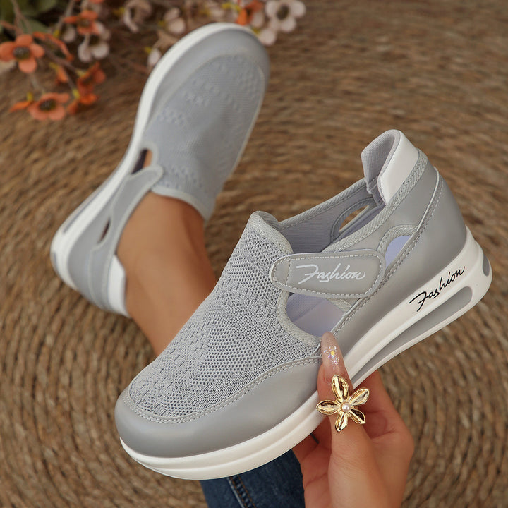 Gray sneakers with white soles held by a hand on a woven surface.