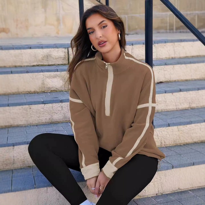 Woman wearing a brown and beige half-zip sweatshirt sitting on steps.