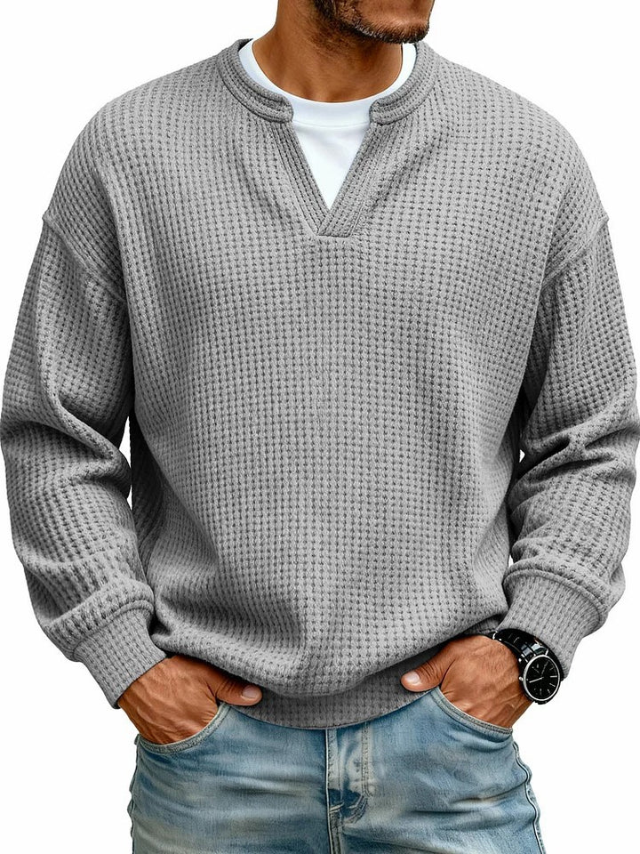 Man wearing a gray textured sweater over a white shirt with blue jeans on a white background