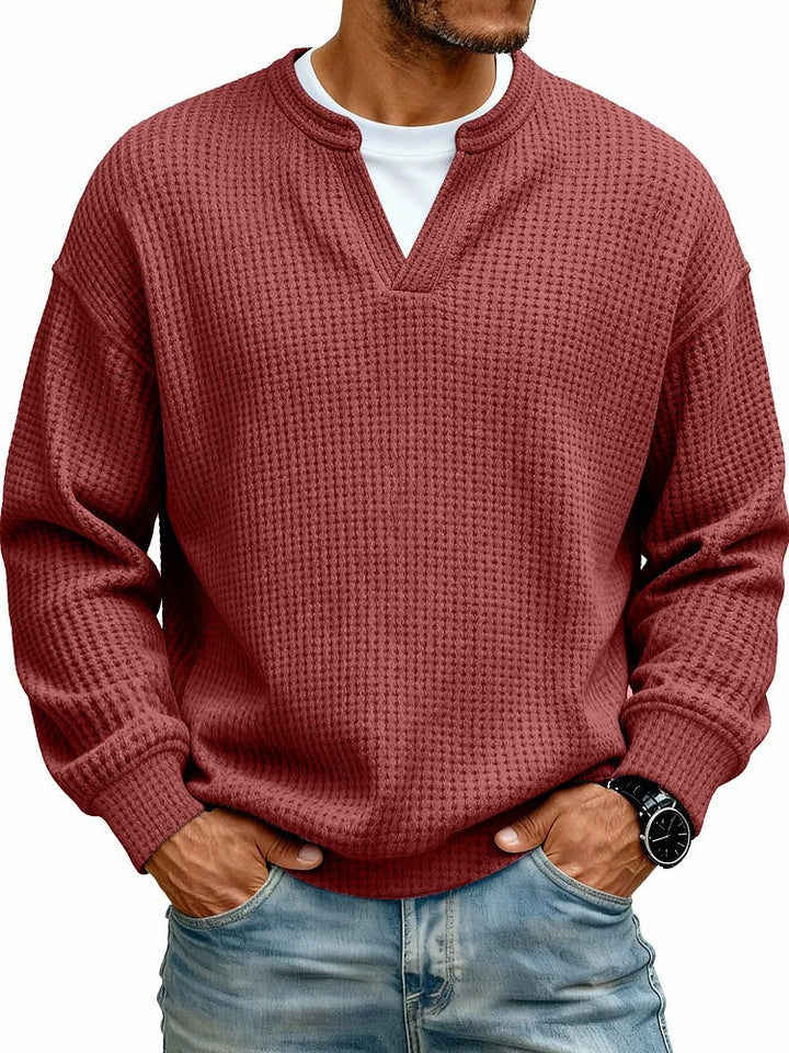 Man wearing a textured red sweater over a white shirt with blue jeans on a white background
