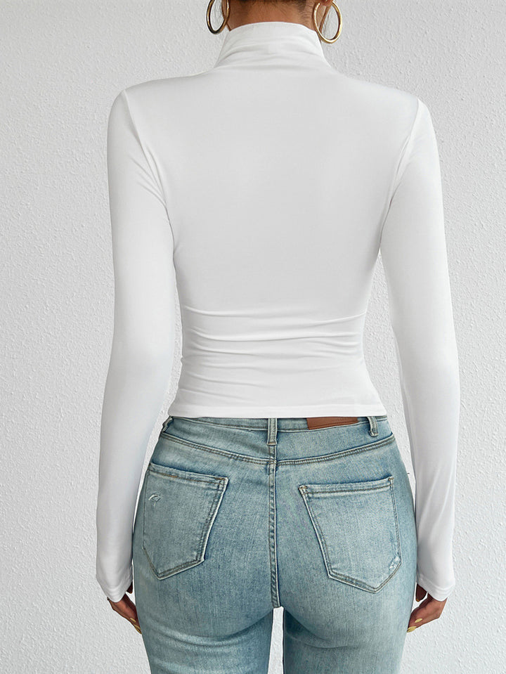 Person wearing a white long-sleeve top and light blue jeans on a plain background