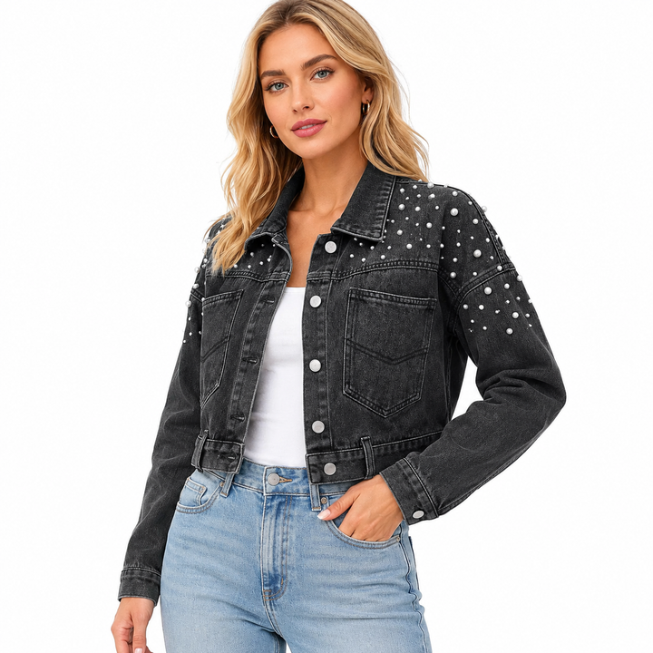 A woman modeling a cropped black denim jacket with silver rhinestone embellishments on the shoulders and sleeves, worn over a white top and light blue jeans against a plain white background.