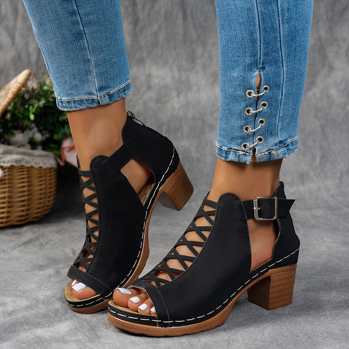 Black open-toe shoes with wooden soles worn with blue jeans on a gray background