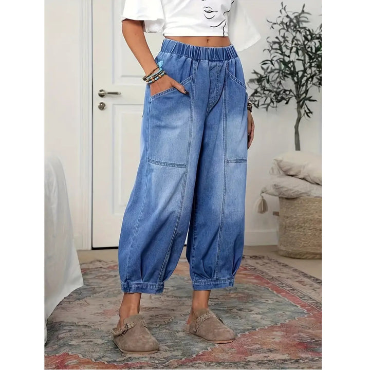 Person wearing blue denim wide-leg pants in a room with a door and plant in the background.