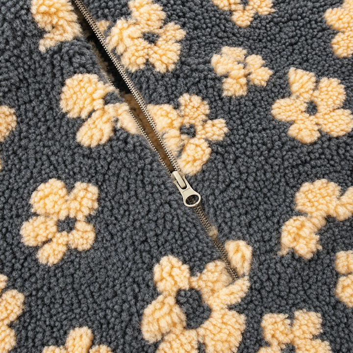 Close-up of a textured fleece or sherpa fabric with a repeating cream floral pattern on a dark charcoal background, featuring a silver metal zipper running diagonally through the center.