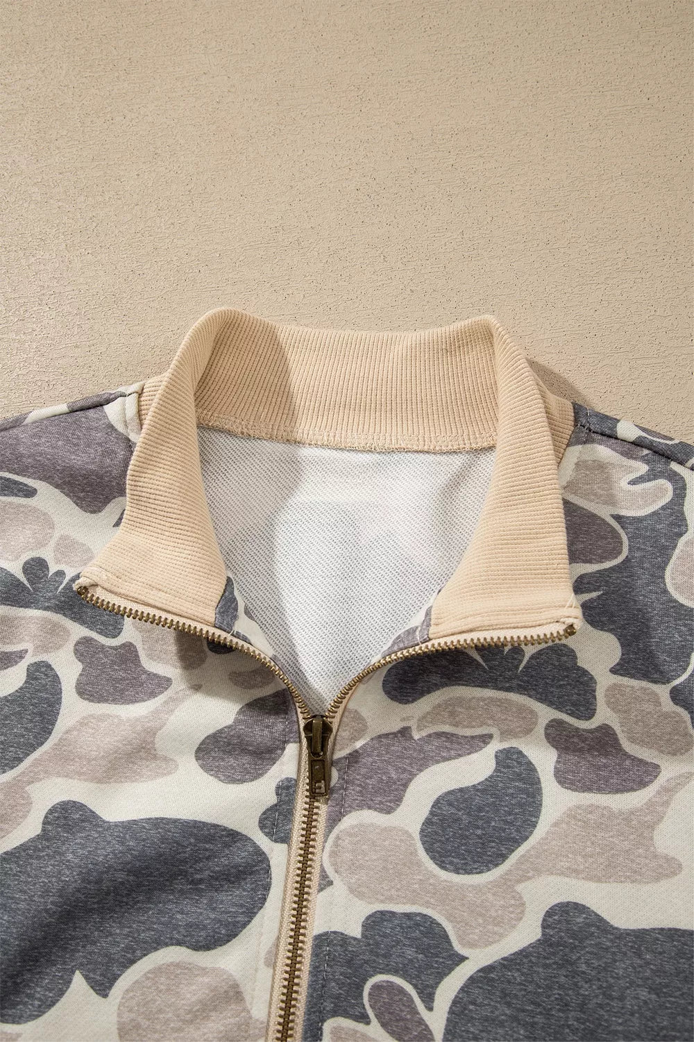 Open bomber neckline showing beige ribbing, inside fabric, a gold-tone zipper and charcoal and taupe camouflage print details