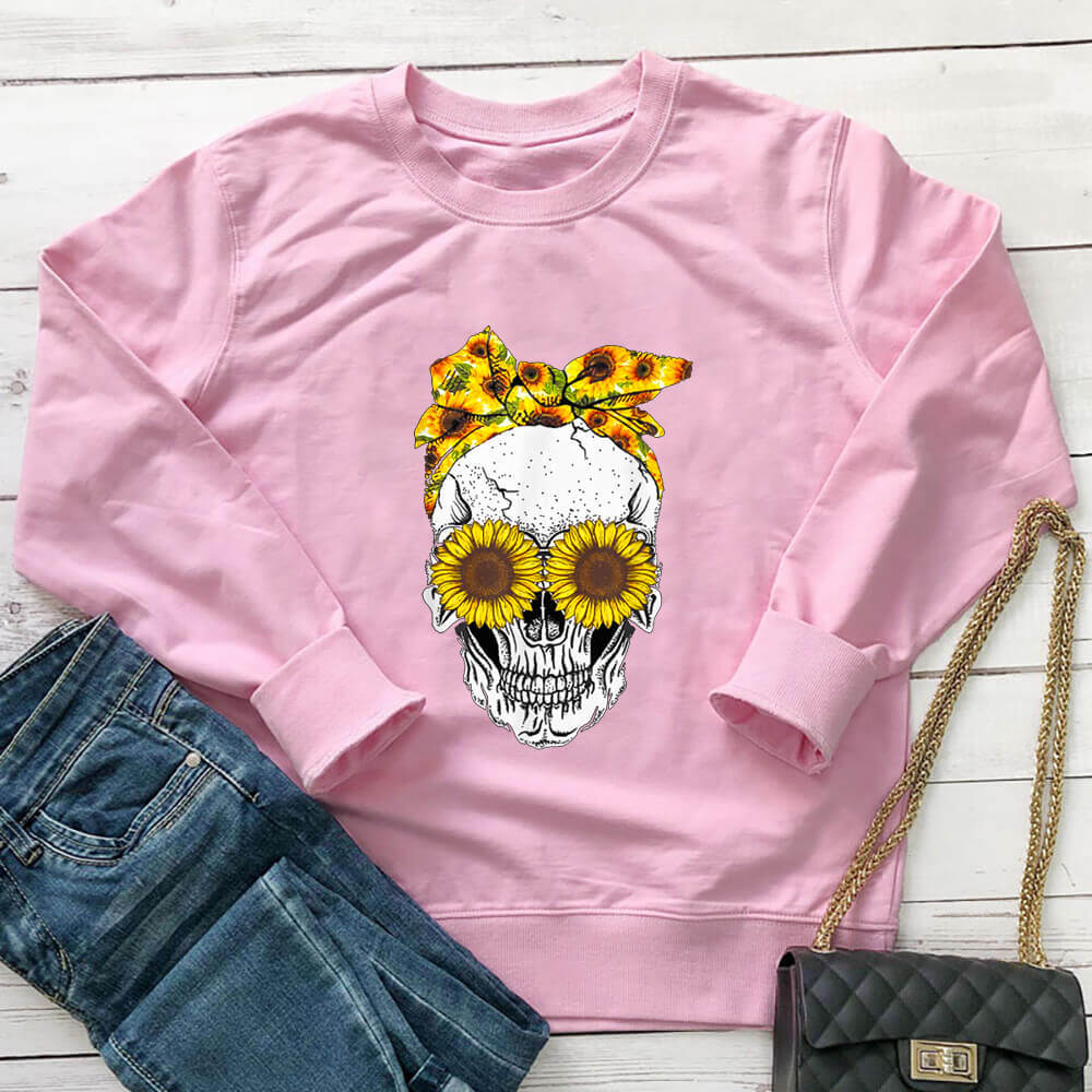 Pink sunflower skull sweatshirt laid flat with jeans and a black handbag