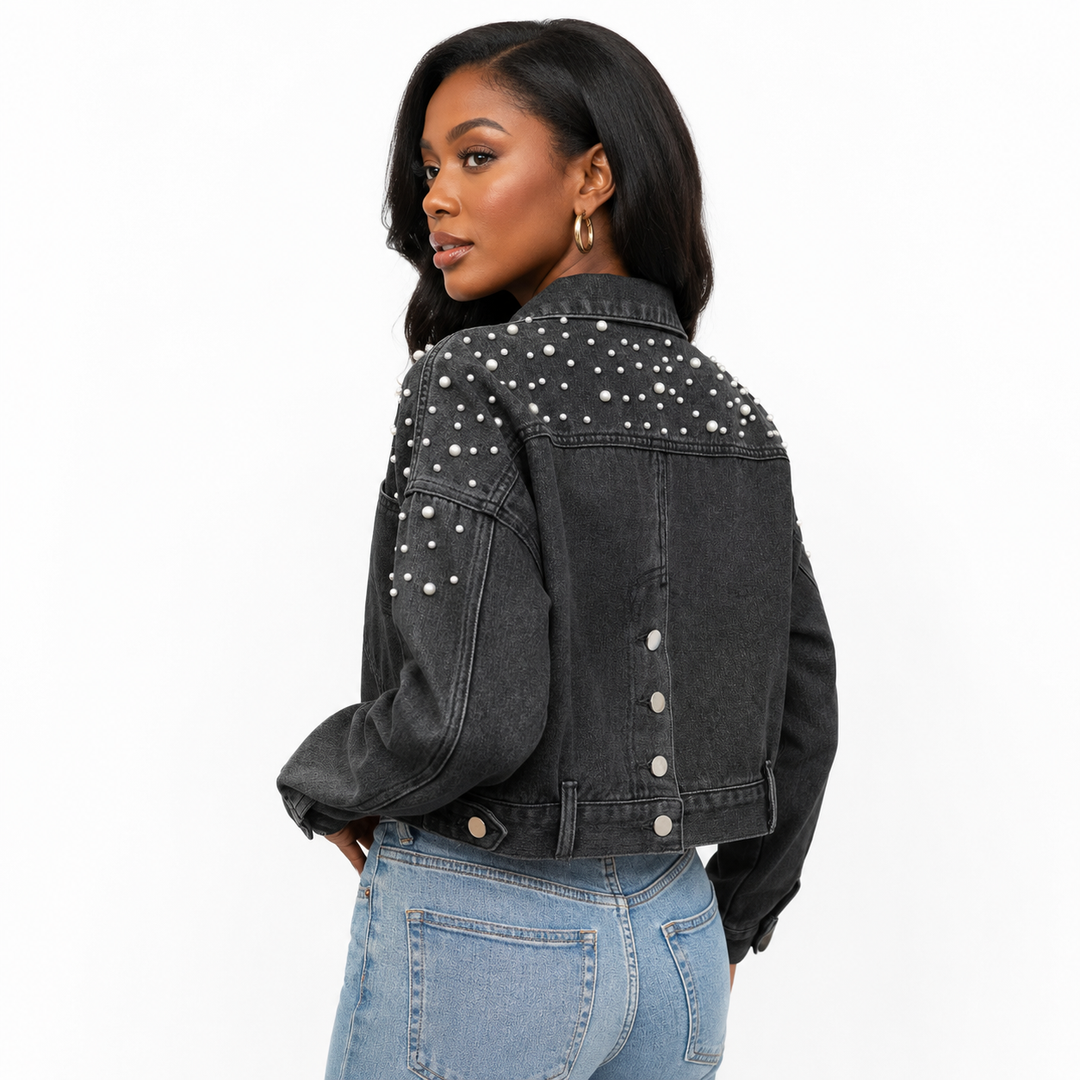 A woman shown from the back wearing a cropped black denim jacket with silver studs across the shoulders and upper back, paired with light blue jeans, against a plain white background.