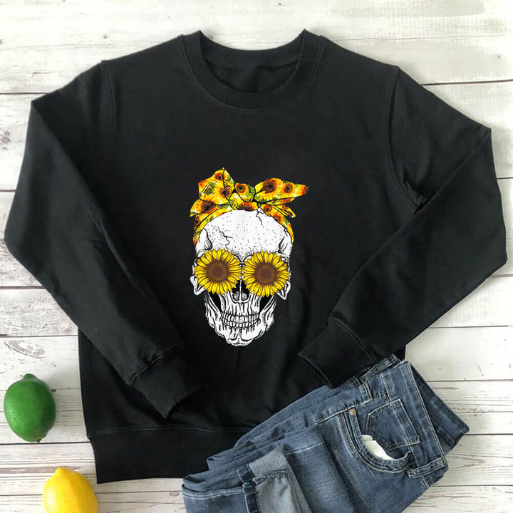 Black sunflower skull sweatshirt laid flat with jeans on a white wood background
