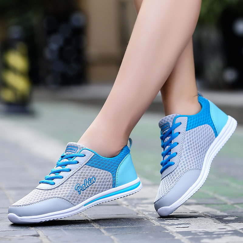 Gray and blue lace-up shoes worn outdoors, showing blue heel panels, gray mesh uppers and white soles beside a stone pavement