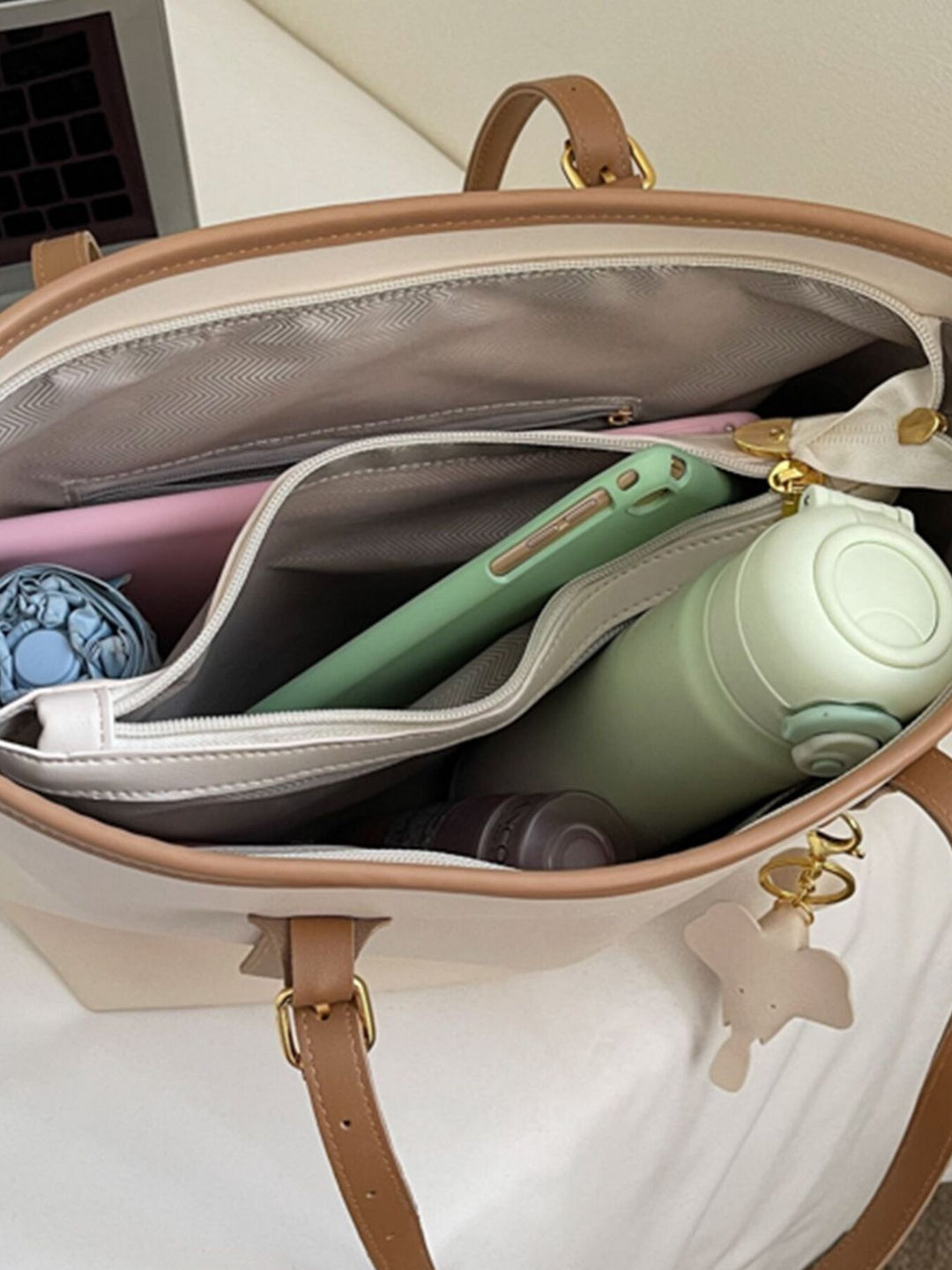 Open beige handbag with various items including a green bottle and pink case.