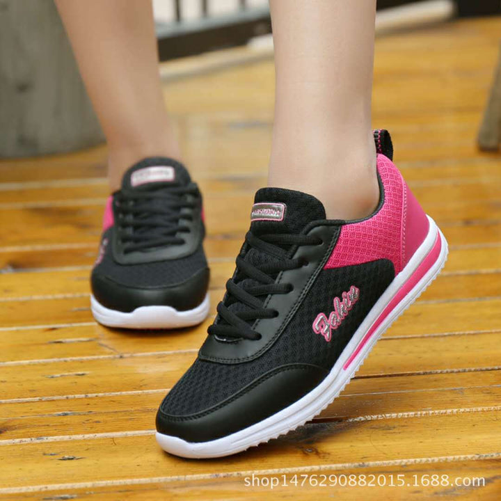Black and pink lace-up shoes worn on wooden steps, showing black laces, pink heel panels, side lettering and flat white soles