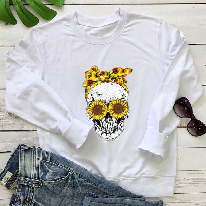 White sunflower skull sweatshirt laid flat with jeans on a white wood background