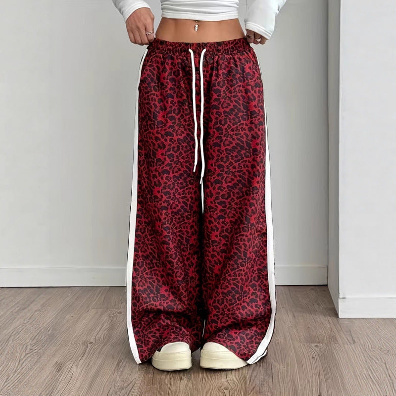 Red leopard print pants with white drawstring and side stripes worn by a person on a wooden floor.