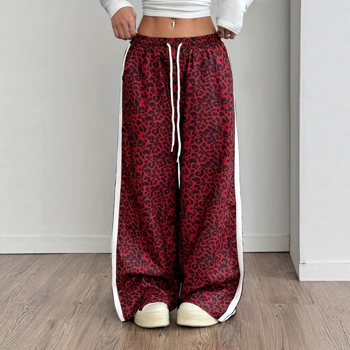 Red leopard print pants with white drawstring and side stripes worn by a person on a wooden floor.