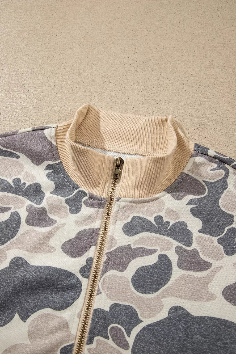 Close view of the beige ribbed bomber collar and closed gold-tone zipper against the cream, charcoal and taupe printed fabric