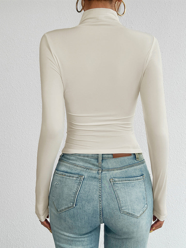 Person wearing a beige long-sleeve top and light blue jeans against a white background
