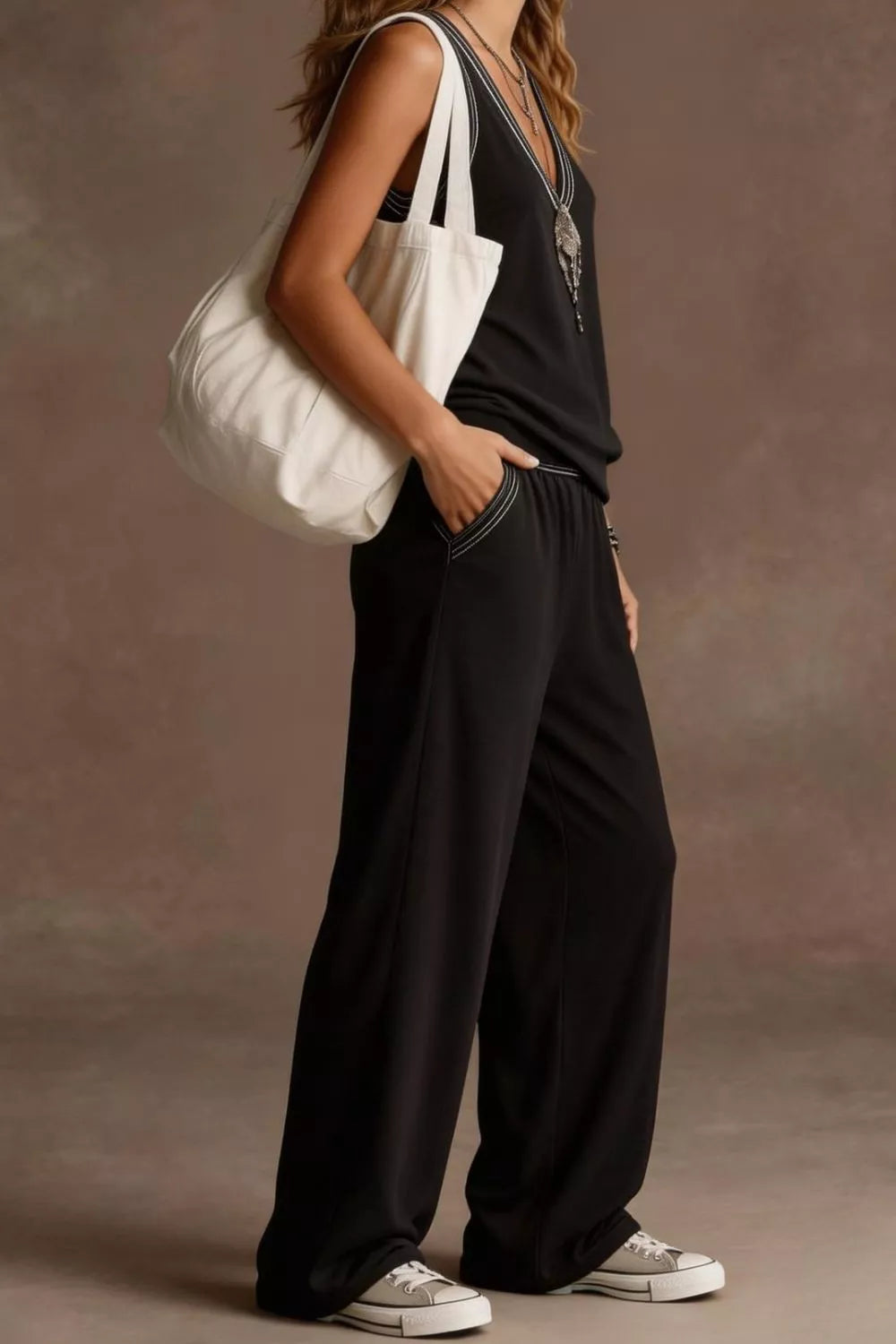 Person wearing a black outfit with a white bag against a neutral background