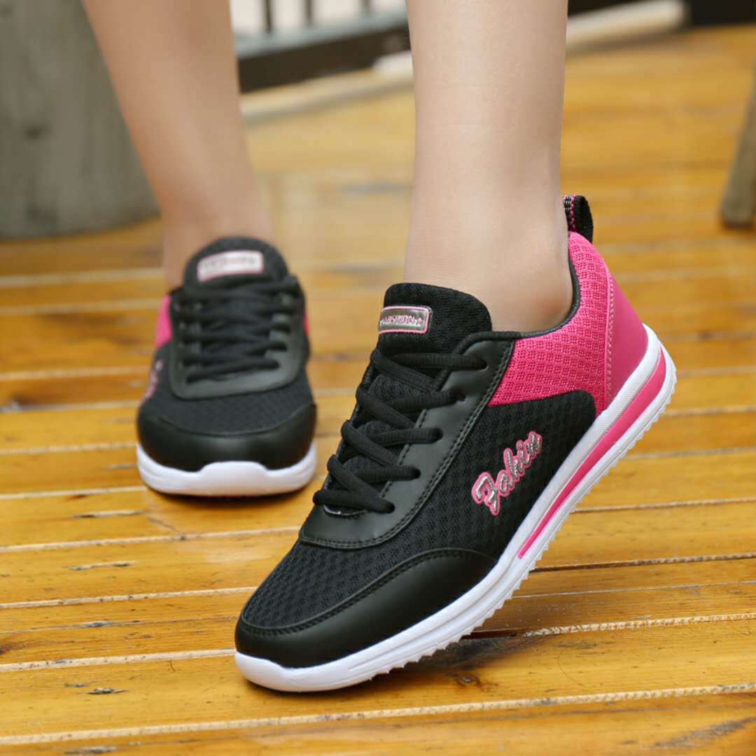 Black and pink lace-up shoes viewed on wooden steps, with black mesh uppers, pink heel panels, white soles and side lettering