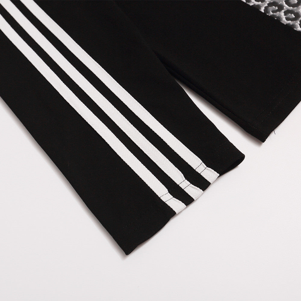 Black polo shirt sleeve detail showing three white stripes, straight sleeve opening and a section of the cross-pattern print.