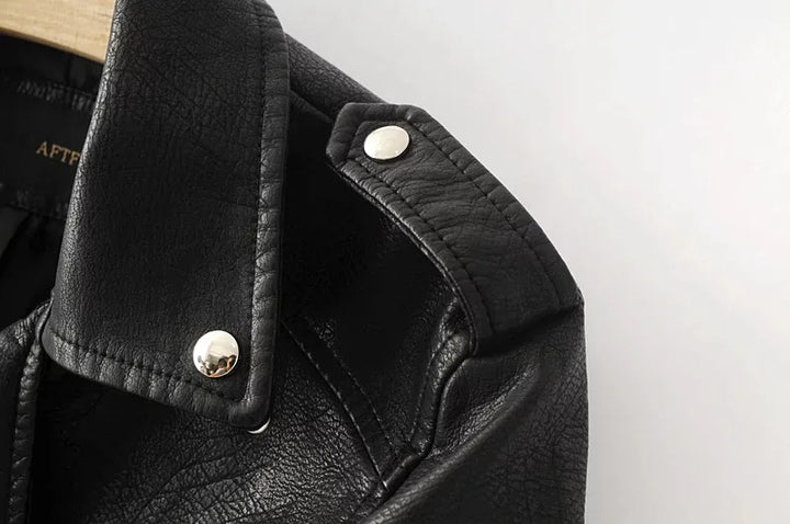 Close-up of the black jacket shoulder tab, showing two round silver-tone snap details, stitched edges and a textured surface.