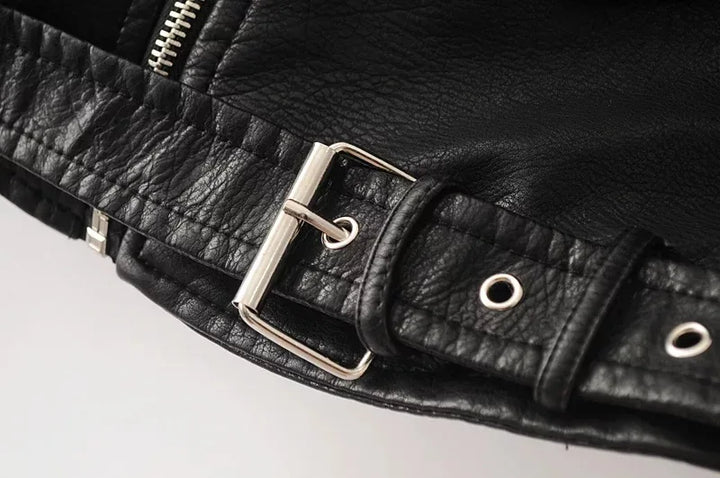 Close-up of the black jacket belt, showing a rectangular buckle, round belt holes, belt loops and the textured outer surface.