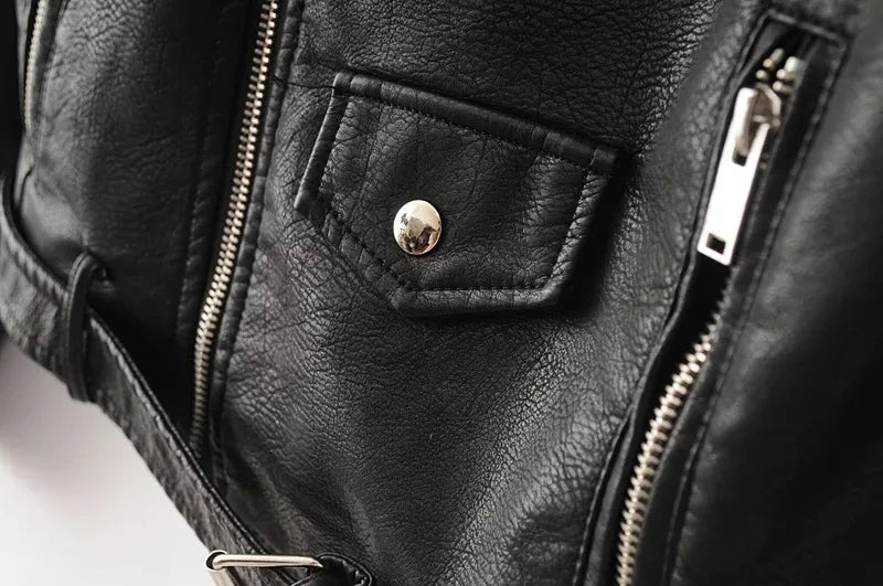 Close-up of black jacket front, showing the small snap-flap pocket detail between the main zip and one vertical lower zipper.