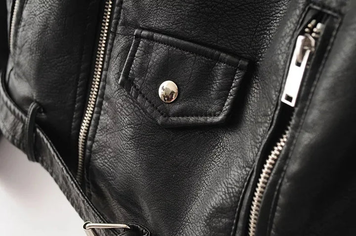 Close-up of black jacket front, showing the small snap-flap pocket detail between the main zip and one vertical lower zipper.