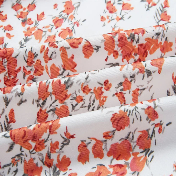 Close-up of Flower White printed fabric, showing small coral-red flowers and fine grey foliage on a white ground shown folded
