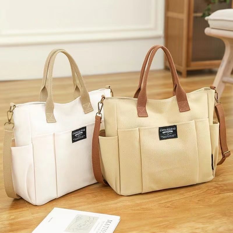 Khaki canvas shoulder bag for women with top handles, adjustable strap and front pocket shown in square product presentation.