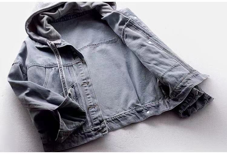 Open blue denim jacket laid flat, showing its inside, grey hood, long sleeves, printed drawstring and a metal button placket.
