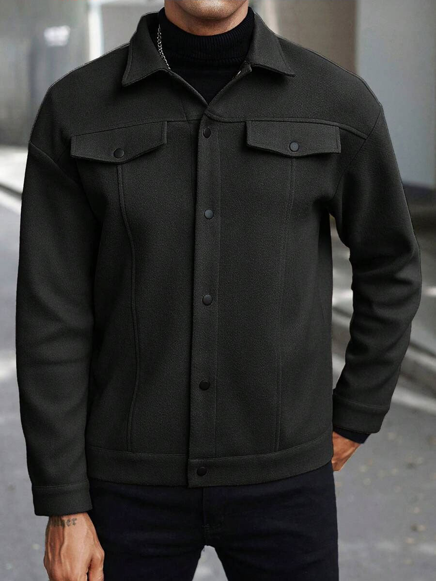 Black jacket on a cropped adult man facing forward, showing pointed collar, chest flap pockets and snapped front on a street.