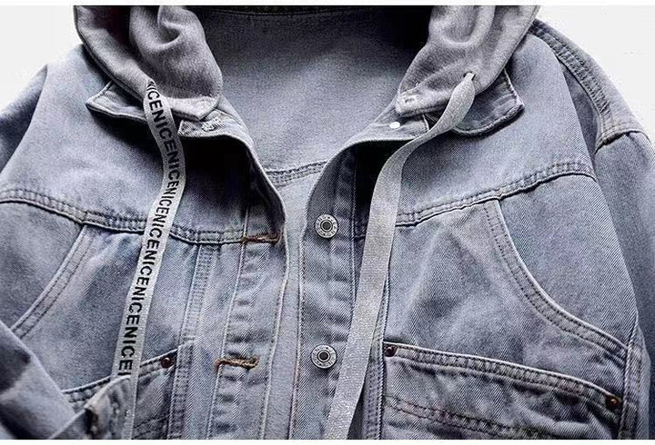 Upper front of a blue denim jacket showing grey hood, printed drawstring, curved pocket openings, and metal button fastening.