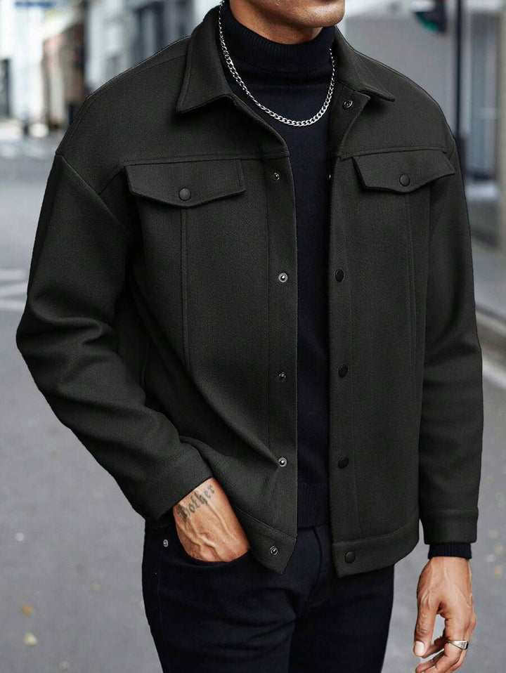 Black jacket on a cropped male model with one hand in a side pocket, showing snap front and chest flap pockets on the street.