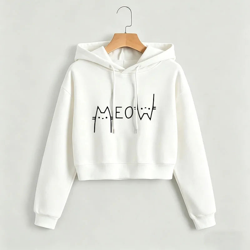 White cropped Meow hoodie on a wooden hanger against a light wall, showing a black cat graphic, hood and long ribbed sleeves.