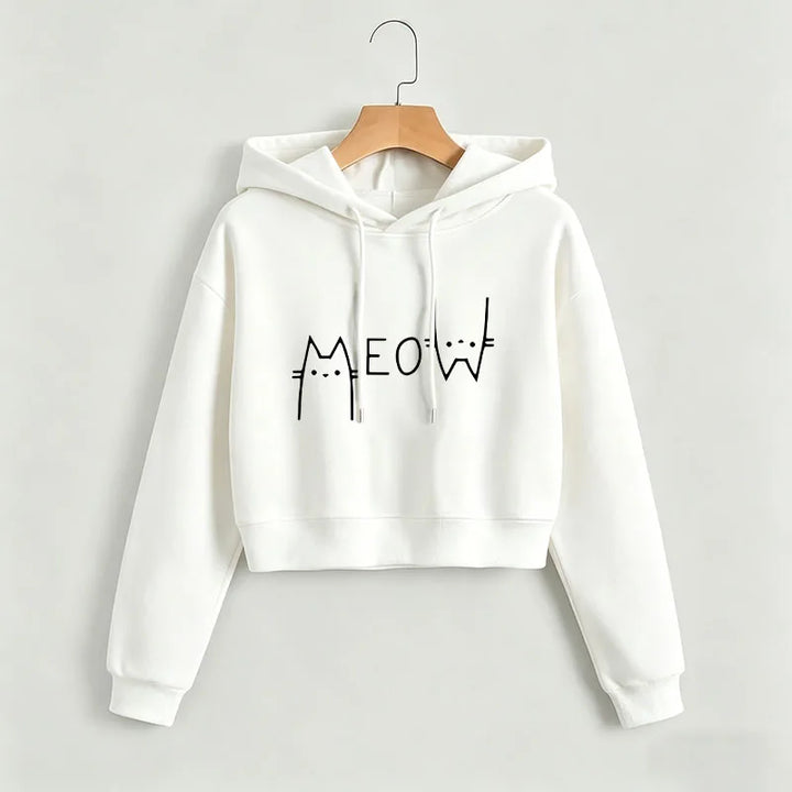 White cropped Meow hoodie on a wooden hanger against a light wall, showing a black cat graphic, hood and long ribbed sleeves.
