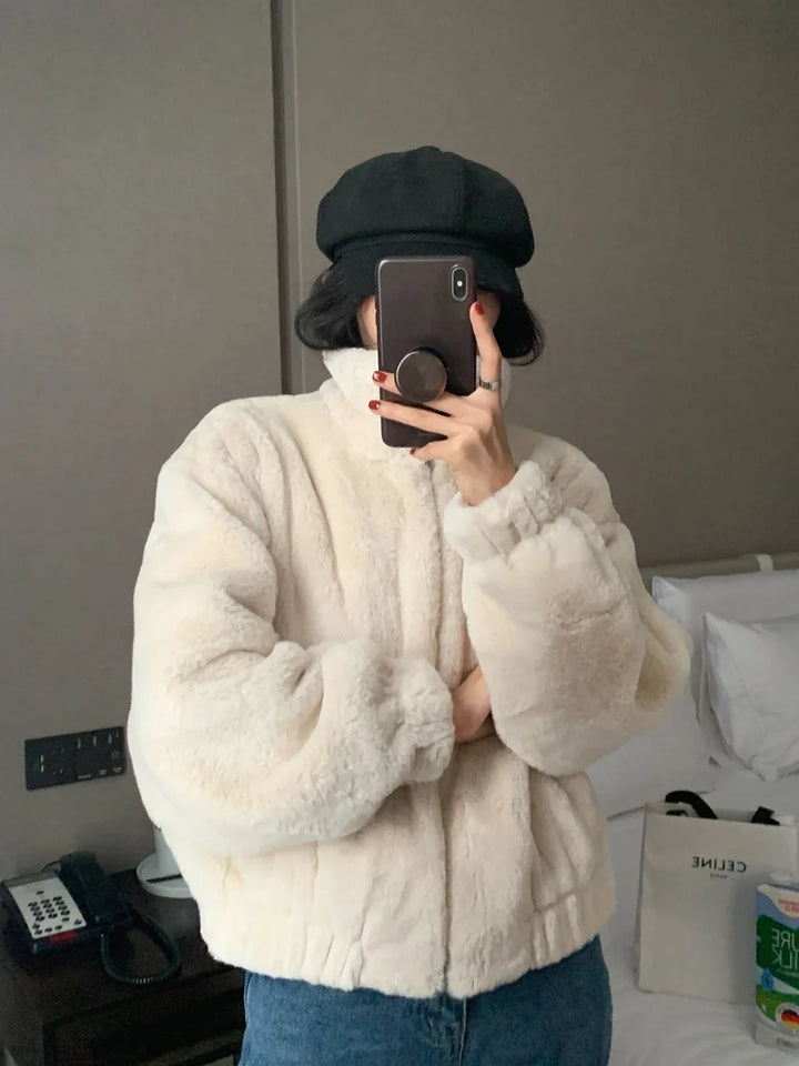Beige plush jacket in a mirror selfie with a black cap, showing the textured surface, a stand collar and full-length sleeves.